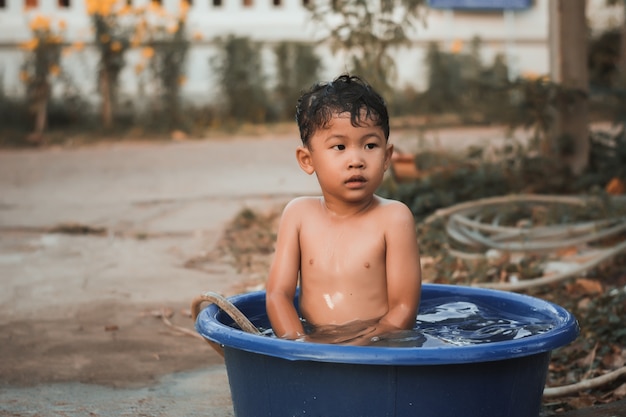 Los niños juegan y bañan agua en el jardín, sentados en un balde de agua.