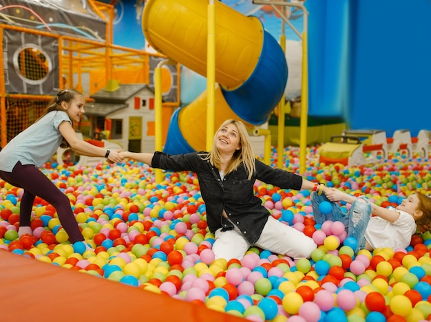 Los niños juegan con la madre en el centro de entretenimiento. Mamá y su hija se divierten en vacaciones, felicidad infantil, niños felices en el patio de recreo