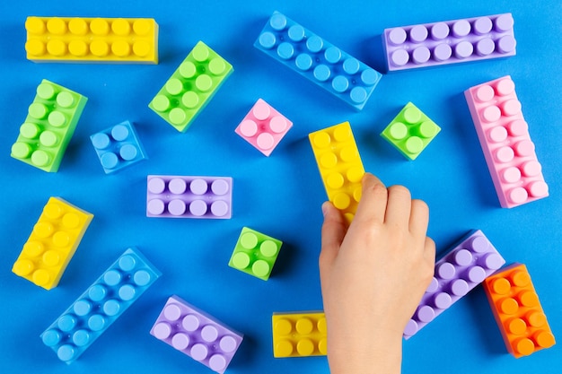 Los niños juegan a mano con coloridos bloques de construcción de plástico sobre fondo azul.