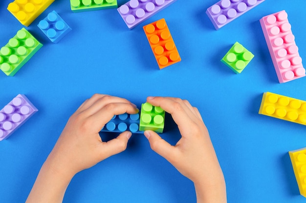 Los niños juegan a mano con coloridos bloques de construcción de plástico sobre fondo azul.