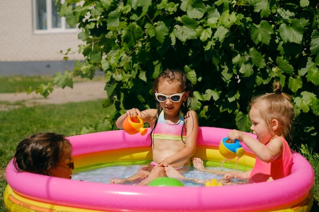 Los niños juegan en una mini piscina inflable con regaderas de juguete regándose unos a otros