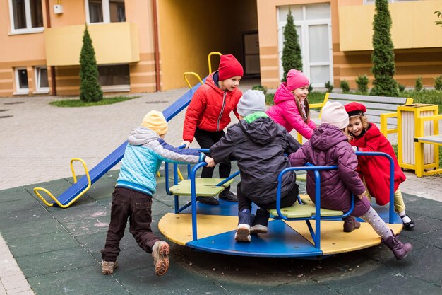 Los niños juegan en el patio de recreo al aire libre en la primavera La niña está sentada en un carrusel Tiempo feliz en el patio de recreo Infancia feliz