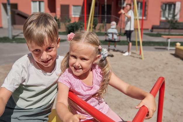 Los niños juegan en el patio de recreo. Los niños y niñas riendo felices se divierten columpiándose y escalando. Actividad al aire libre