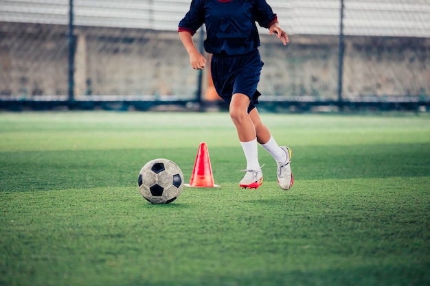 Niños jugando al cono de tácticas de pelota de fútbol de control en un campo de hierba con antecedentes de entrenamiento