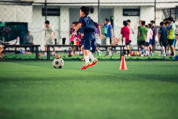 Niños jugando al cono de tácticas de pelota de fútbol de control en un campo de hierba con antecedentes de entrenamiento