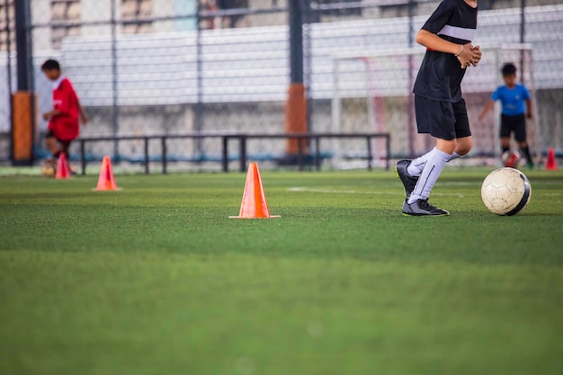 Niños jugando al cono de tácticas de pelota de fútbol de control en un campo de hierba con antecedentes de entrenamiento