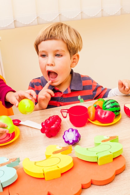 Niños jugando con artículos para el hogar y frutas artificiales en el jardín de infantes.