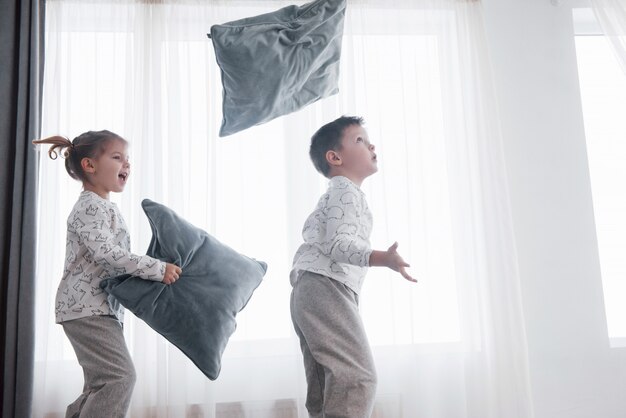 Niños jugando en la cama de los padres. Los niños se despiertan en el soleado dormitorio blanco.