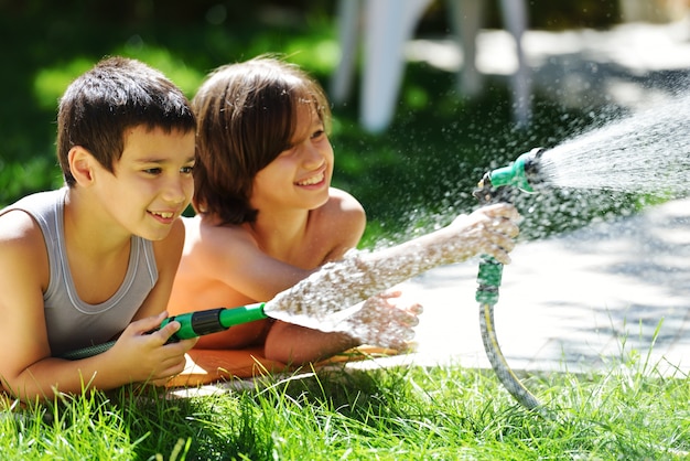 Niños jugando y chapoteando con rociadores de agua en el patio de césped de verano