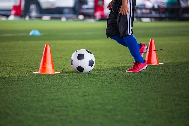 Niños jugando cono de tácticas de balón de fútbol de control en campo de hierba para entrenamiento