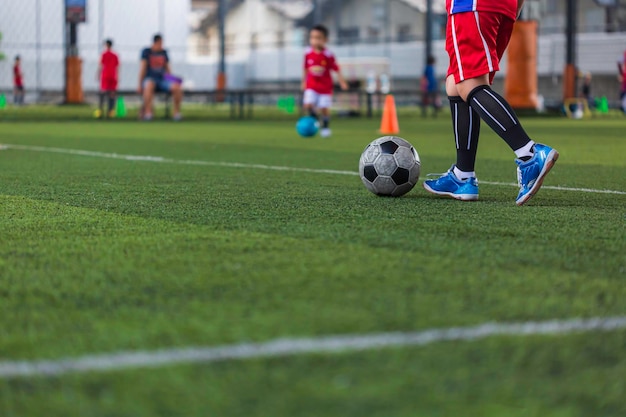 Niños jugando cono de tácticas de pelota de fútbol de control en campo de hierba con antecedentes de entrenamiento