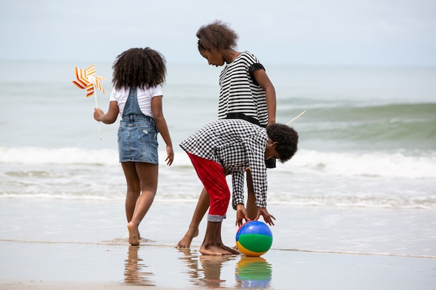 Niños jugando corriendo sobre la arena en la playa, un grupo de niños tomados de la mano en una fila en la playa en verano, vista trasera contra el mar y el cielo azul