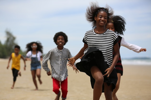 Niños jugando corriendo sobre la arena en la playa, un grupo de niños tomados de la mano en una fila en la playa en verano, vista trasera contra el mar y el cielo azul