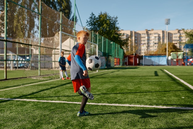 Niños jugando fútbol, joven futbolista con uniforme golpeando la pelota. Estadio al aire libre de la escuela