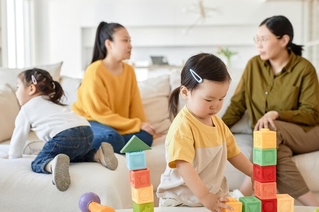 Niños jugando juguetes mientras sus madres hablan de fondo en la sala de estar