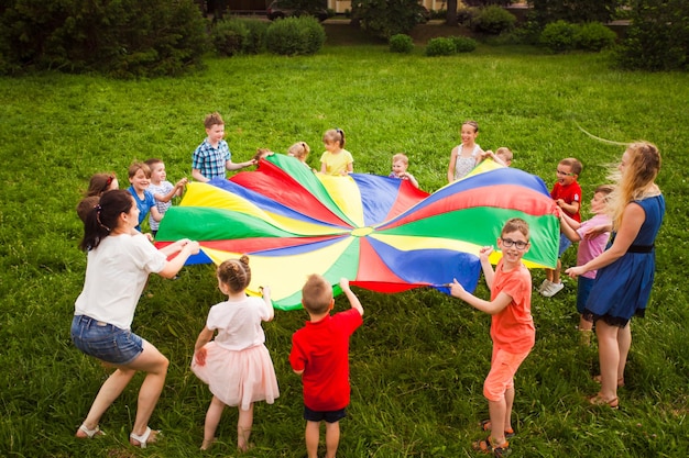 Niños jugando con paracaídas de arco iris en el parque durante el campamento de verano