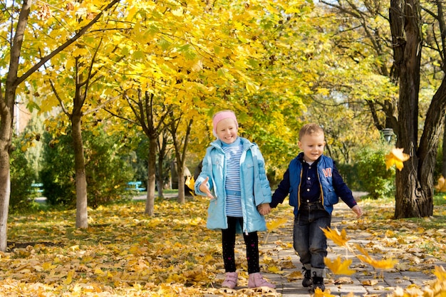 Niños jugando en el viento con coloridas hojas de otoño amarillas