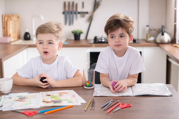 Niños junto con lápices de colores y plastilina en la mesa de ocio en casa.