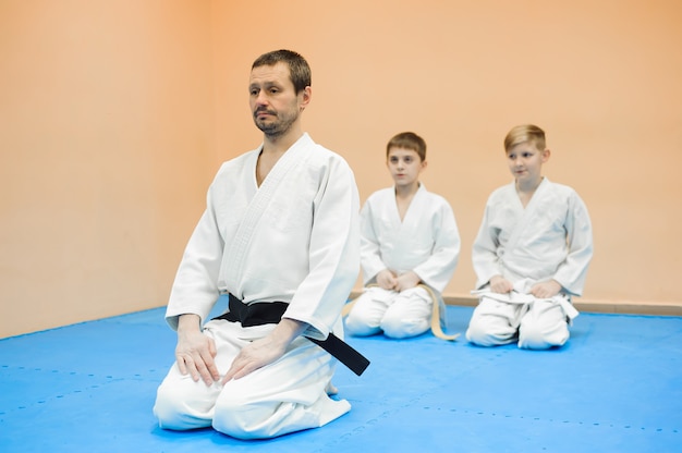 Los niños en kimono se sientan en el tatami con un entrenador en un seminario sobre artes marciales