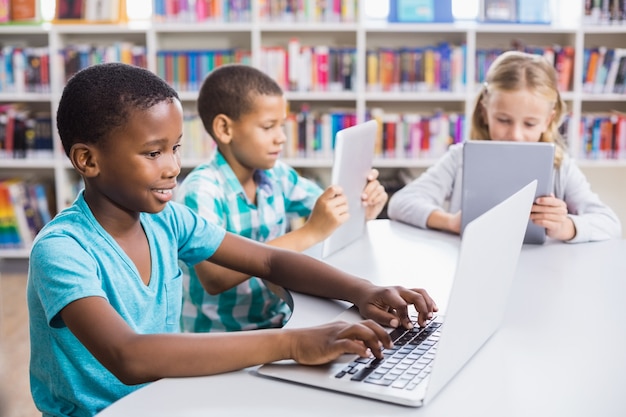 Niños con laptop y tableta digital en la biblioteca