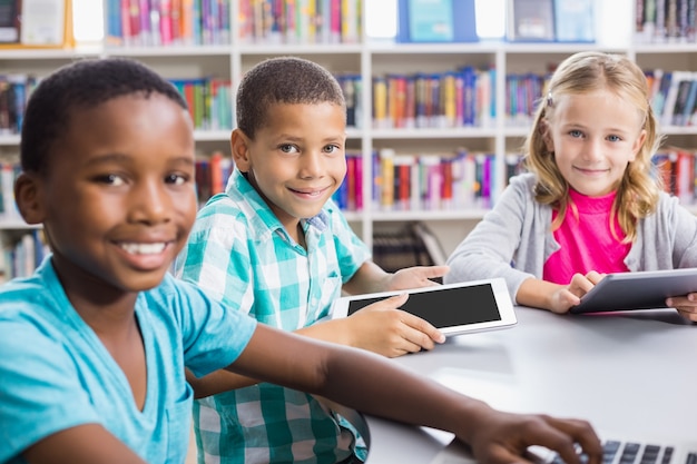 Niños con laptop y tableta digital en la biblioteca