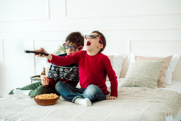 Niños lindos comiendo palomitas de maíz mientras ven la televisión en casa en vasos 3 d.