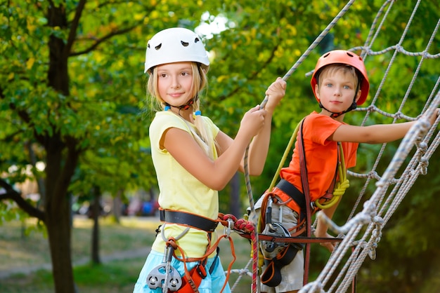 Niños lindos con equipo de escalada en un parque de aventuras.