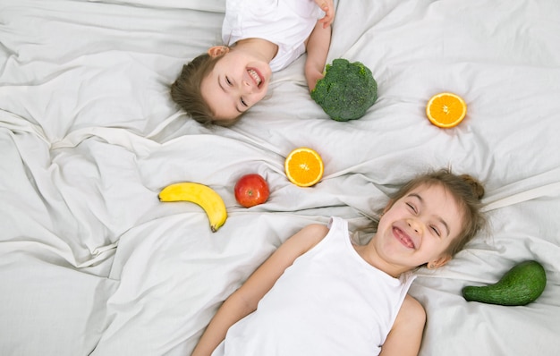 Los niños lindos felices juegan con frutas y verduras sobre un fondo claro. Alimentos saludables para niños.