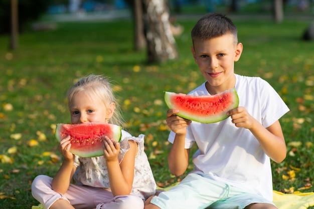 A los niños lindos lttle niño y niña comiendo sandía jugosa en el picnic en el prado del parque de otoño.