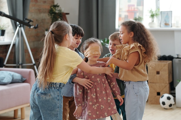 Niños lindos que rodean a una de las niñas con los ojos atados durante el juego