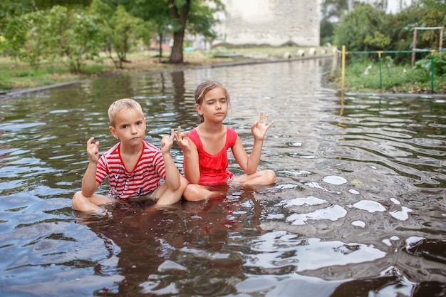 Niños lindos saltando y nadando en los charcos después de la cálida lluvia de verano infancia feliz