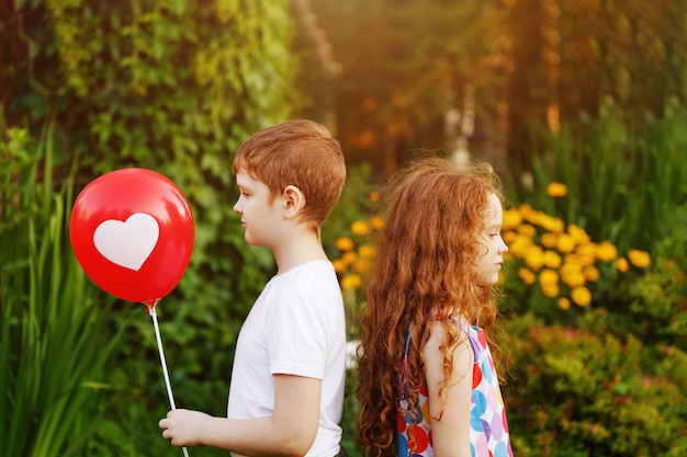 Los niños lindos sostienen los globos rojos con el corazón en parque del verano.