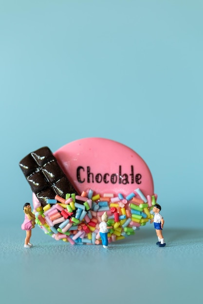 Niños en miniatura con galleta de chocolate de pie contra un fondo azul Concepto del Día Mundial del Chocolate