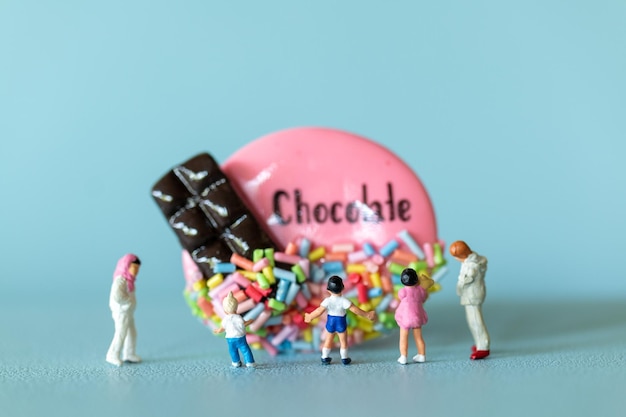 Niños en miniatura con galleta de chocolate de pie contra un fondo azul Concepto del Día Mundial del Chocolate