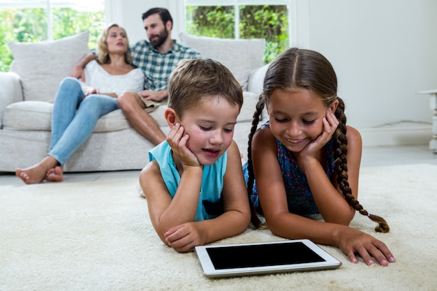 Niños mirando la pantalla de la tableta digital mientras los padres en segundo plano.