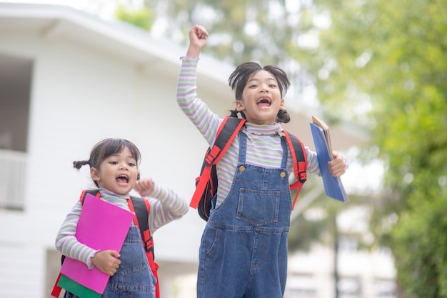 Niños con mochilas saltando en el parque cerca de la escuela. Alumnos con libros y mochilas al aire libre