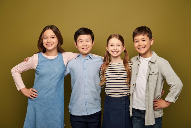 Niños multiétnicos sonrientes abrazando a amigos con ropa casual mirando a la cámara juntos y posando