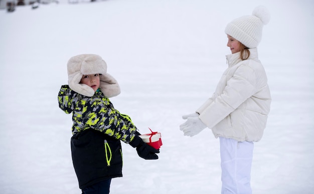 Foto niños en la nieve, un niño pequeño con ropa de invierno le da un regalo en forma de corazón a una niña