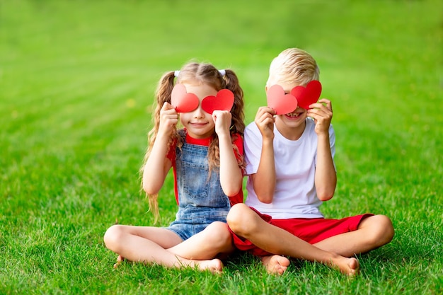 Los niños, una niña y un niño rubio, cerraron los ojos con corazones en verano en un césped sobre hierba verde, el concepto de un espacio de vacaciones de San Valentín para texto