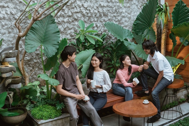 Niños y niñas asiáticos charlando y disfrutando de un café mientras están sentados en la mesa y el banco de madera en el jardín de su casa