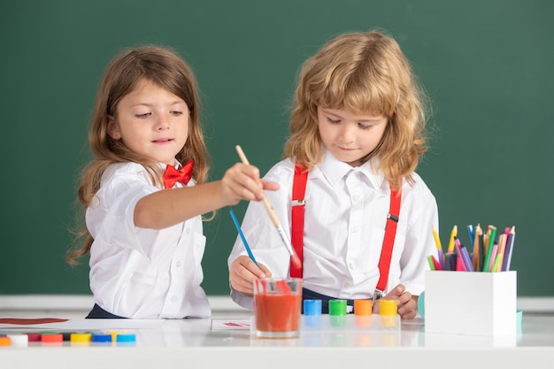 Niños y niñas de la escuela de educación de la primera infancia pintando con pinturas de color y pincel en clase