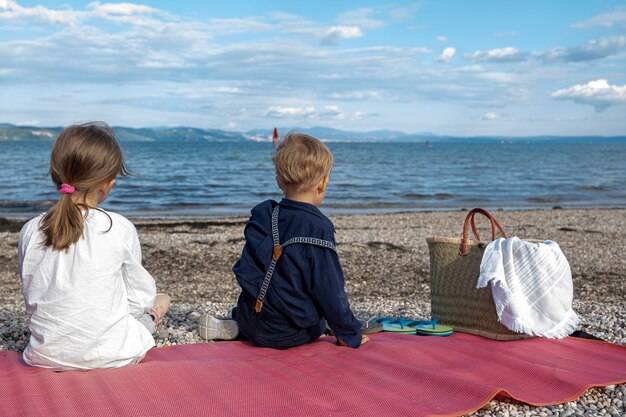 Los niños y las niñas están sentados en una playa rocosa con el telón de fondo de un hermoso cielo