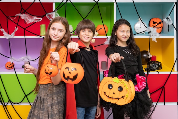 Foto niños y niñas felices parados frente a la decoración de la fiesta de halloween y sosteniendo calabaza jacko'lantern