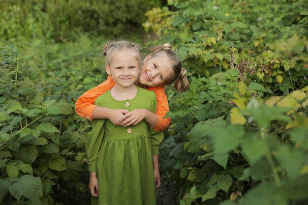 Los niños niñas rubias en un abrazo de vestido amarillo y verde con el telón de fondo de un jardín de amigos