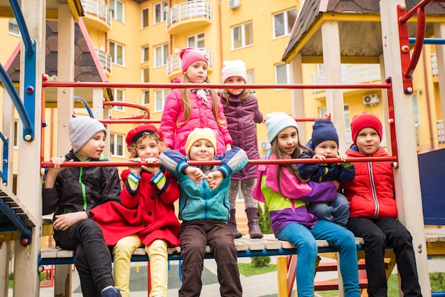 Niños y niñas sentados juntos en el patio de recreo Niños con ropa cálida y colorida jugando al aire libre a principios de la primavera