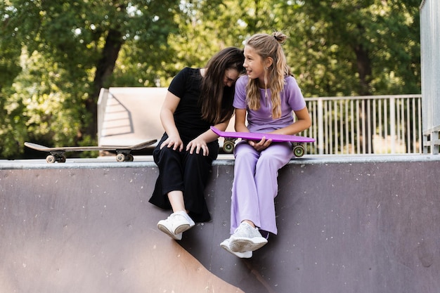 Los niños niñas sonríen, ríen y se divierten juntos Los niños con patinetas y tableros de centavos se comunican y discuten en el patio de recreo deportivo Concepto de amistad de niñas