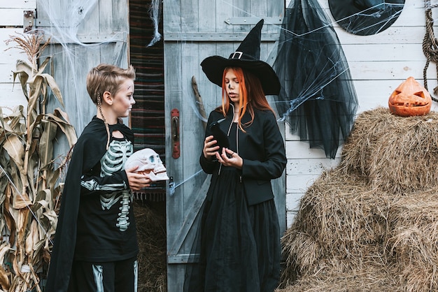 Los niños un niño con un disfraz de esqueleto y una niña con un disfraz de bruja divirtiéndose en una fiesta de Halloween en el porche decorado