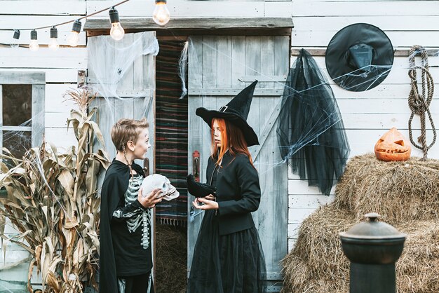 Los niños un niño con un disfraz de esqueleto y una niña con un disfraz de bruja divirtiéndose en una fiesta de Halloween en el porche decorado