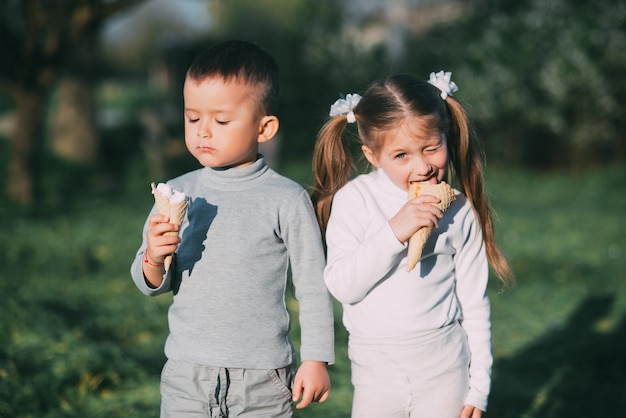 Niños niño y niña comiendo helado al aire libre sobre césped y árboles de fondo muy dulce