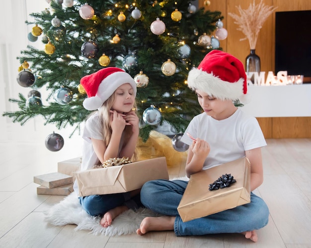 Niños: un niño y una niña juegan cerca del árbol de Navidad. Interior de la sala de estar con árbol de Navidad y adornos. Año nuevo. Dar regalos.